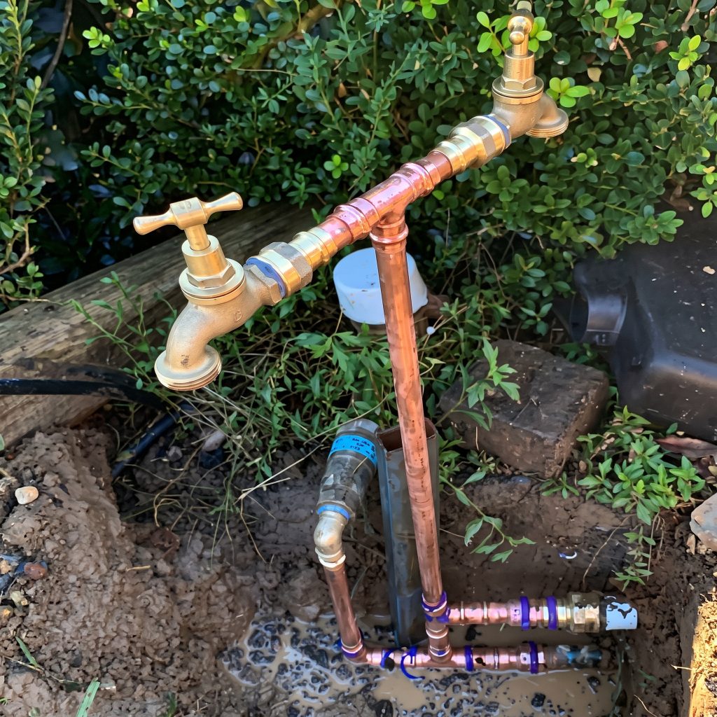 Copper water pipe with brass garden taps rising from the soil