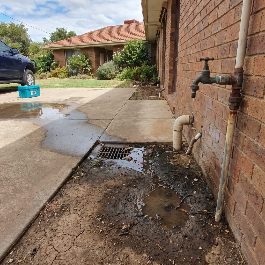 Water leaking from an outdoor tap onto the path beside a brick home